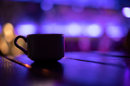Cup on table in purple. Silhouette of cup in dark room. Mug with drink. Dishes on table.
