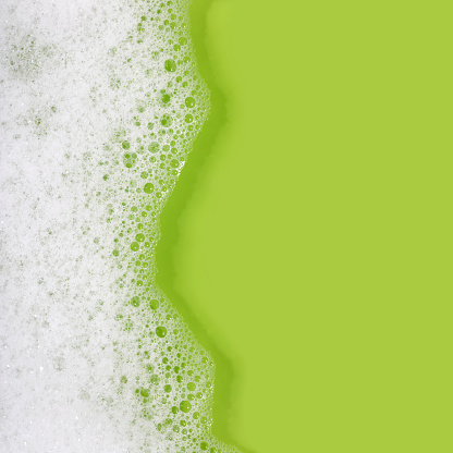 Close-up of soap suds with water on a green background. Space for copy.