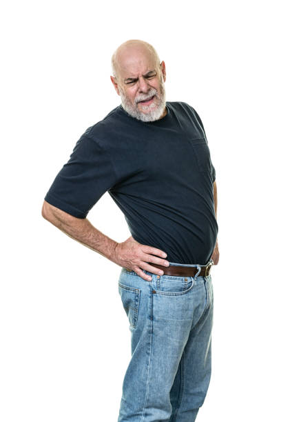 Muscular senior adult man with back and hips aches and pains is grimacing as he twists his upper body to stretch his back muscles while pushing and massaging his hips with his hands as he tries to get more comfortable. White background.