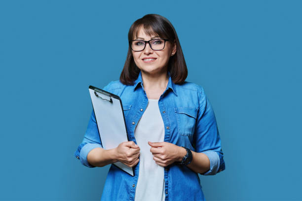 istock Middle aged woman with clipboard looking at camera on blue background 1451552432