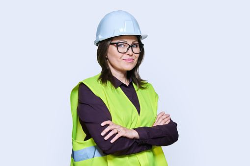 Portrait of female industrial construction worker in hardhat vest looking at camera with crossed arms on white background. Logistics construction industry management architecture engineering staff