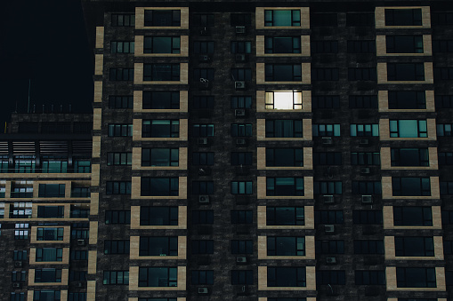 Facade of a modern apartment building in blackout. One window lights up in the house. Apartment building without electricity at night