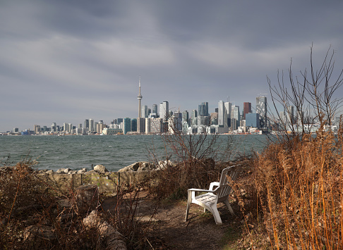 A  white Adirondack chair on Ward's Island with a view across the Inner Harbour to downtown Toronto. Windy morning on the Toronto Islands by Lake Ontario.