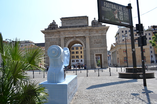 Milan, Italy - June 7, 2015: View from the  Fashion Street Corso Como to the Ancient Porta Garibaldi City Gate and the Sewing Machine Sculpture of the Fashion Brand Camicissima on a Sunny Day.