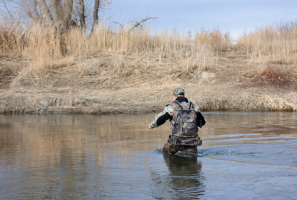 Hunter (trapper) in camouflage crossing a shallow river