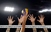 Close up of Volleyball spiking and hand blocking over the net under bright spotlights