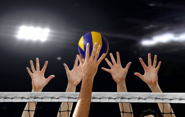 close up of volleyball spiking and hand blocking over the net under bright spotlights - volleyball volleying human hand men imagens e fotografias de stock