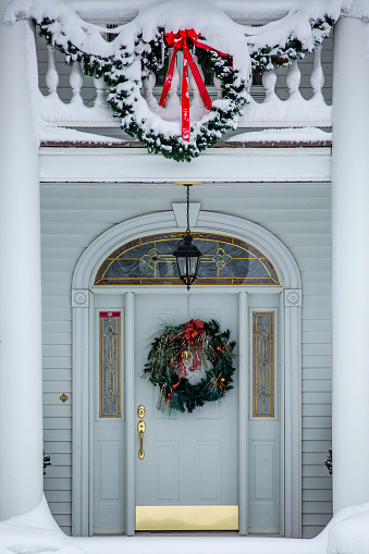 Gold and white front door decorated with Christmas decorations and snow, vertical