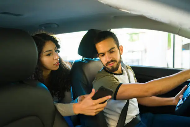 Mexican driver looking at the directions of a passenger while on a ride-share service car