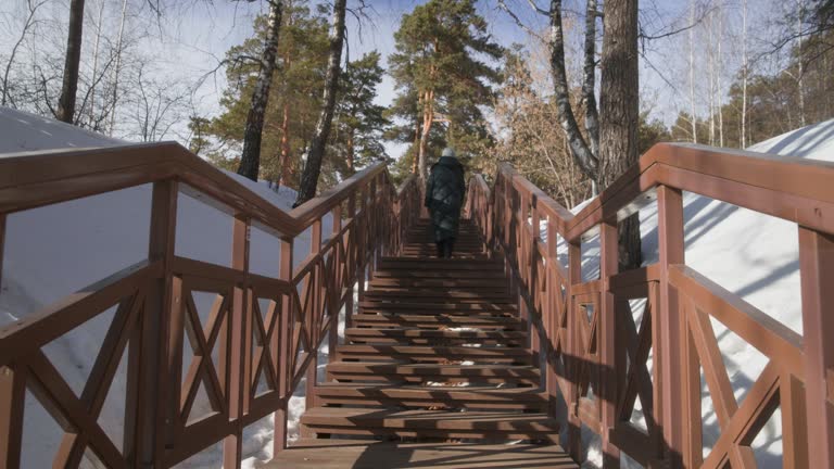 Woman walks in winter park climbs up wooden stairs, cardio, fitness training.