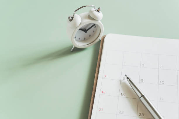 istock top view of pen on white open planner with a light green background and blurred clock in soft focus. For planning business, working space concept 1451636352
