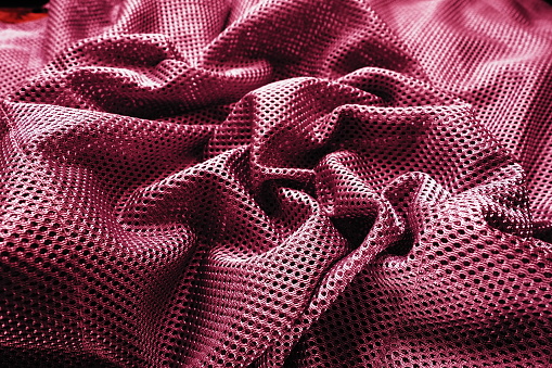 Synthetic fabric with holes, laid in waves and twisted into folds. Beautiful drape. Fabric for curtains, interior design, and decor. Twisted or wrinkled red burgundy porous fabric.