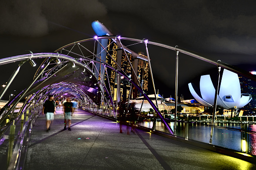 People walking on the Helix Bridge, a pedestrian bridge linking Marina Centre with Marina South in the Marina Bay area in Singapore. In the distance, the Artscience Museum and the Marina Bay Sands.