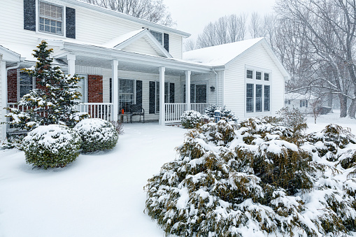 Suburban house with snow on the ground and more falling