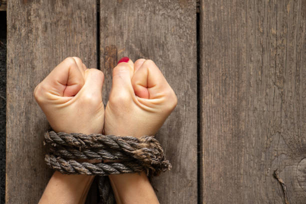 tied female hands with rope on wooden background close-up stock photo