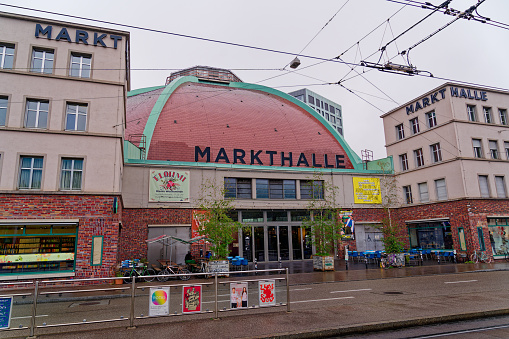 Entrance of Markthalle (Market Hall) with tram station in the foreground at City of Basel on a rainy and gray autumn day. Photo taken October 3rd, 2022, Basel, Switzerland.