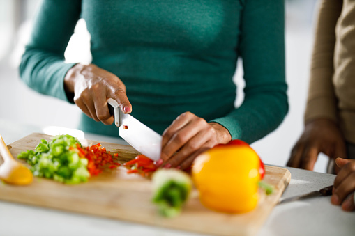 Close up of unrecognizable African American woman cutting peppers in the kitchen.