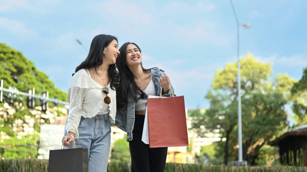 Image of two young asian women talking, spending time together while walking in the shopping district of a city. stock photo