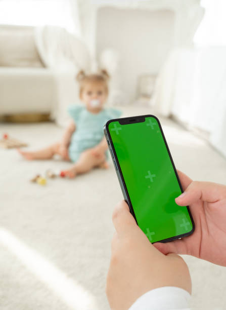 Young mom shopping online on website using smartphone green screen while play with child. Woman search for products for children in Internet. Working from home. App for kids goods. Close-up. Vertical