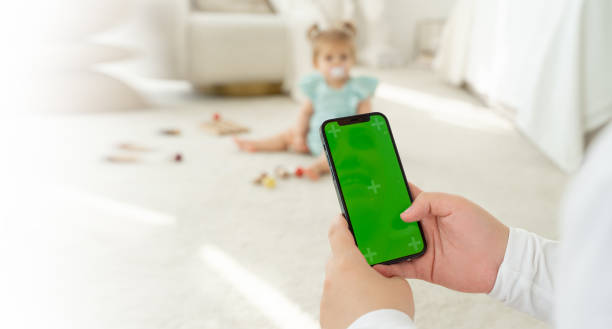 istock Young mom shopping online on website using smartphone green screen while play with child. Woman search for products for children in Internet. Working from home. App for kids goods. Close-up. Back view 1451695441