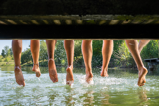 Rear view of three friends dangling their feet off a wooden pier.