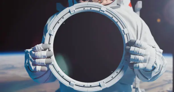 An astronaut with a round plate with trackers  for your title. Astronaut against the Earth. Spacemman holding a round plate with chromakey in his hands