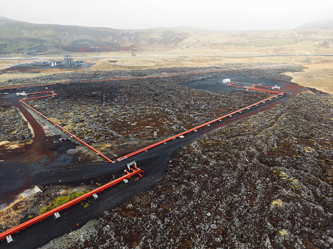 Geothermal Power Plant, hot water power station in Iceland. Steam rolling out of the plant chimneys, red large tubes running across the grounds filled with hot water. Sustainable, energy efficient Cloudy cold autumn day in Iceland.