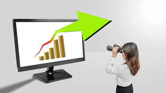 Asian businesswomen with binoculars looking at increasing graphs on the monitor screen