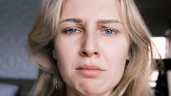 Portrait of crying grieving woman 30 years old. Grimace of sadness with tears in her eyes and twisted chin of blonde woman looking at camera. Emotional swings, unstable psyche, mental problems