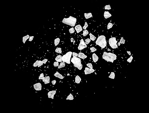 Toma macro de cristales de sal que caen y vuelan aislados sobre negro photo