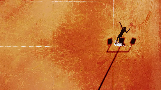 Tennis court drone aerial shot vertical top view, overhead shot of a player shadow silhouette tennis player on a juicy red coating