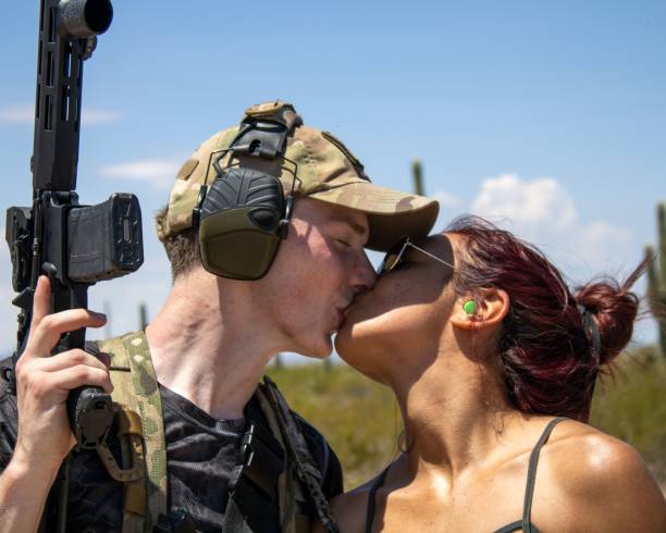 istock Interracial couple kissing while holding assault rifles in Arizona desert 1451741981