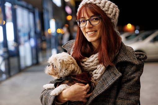 Young woman sitting on bench and holding dog in lap in the city at night