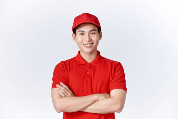istock Smiling delivery man in red uniform standing with arm crossed - isolated on white background 1451744865