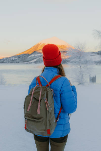 istock Woman with backpack walking by the scenic winter lake with mountain view during sunset in Norway 1451748310