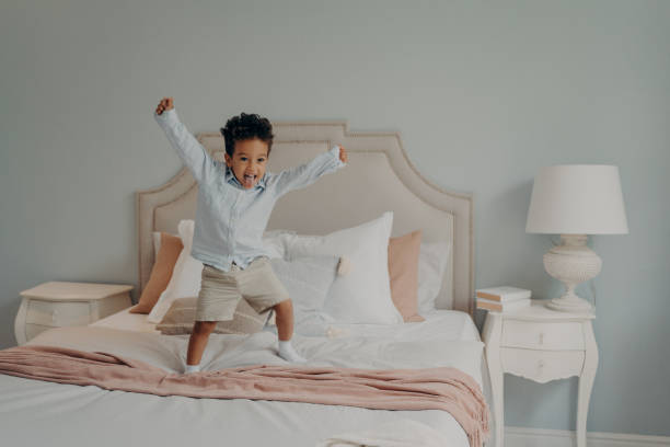 istock Adorable cute kid jumping cheerfully on bed and having fun at home 1451748336