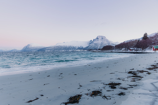Dramatic frozen sunset by the ocean with snowy mountain range in Scandinavia