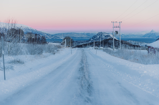 Dramatic view from the car of the snowy mountain pass leading down to the sea during winter pink sunset in Scandinavia
