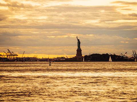 Statue of liberty silhouette against golden cloudy sky in New York City. Sunset time in New York.
