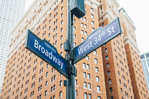 Broadway and West 34th St signs in New York City. Brick building in the background. Crossroads in Manhattan.