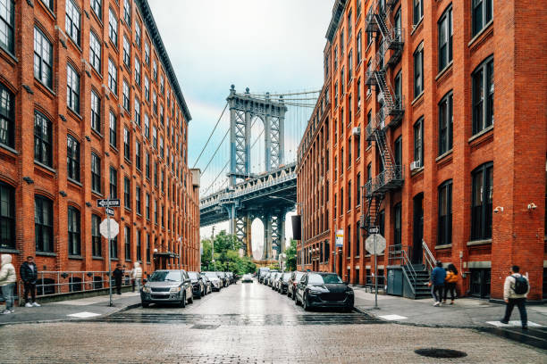 Dumbo district view in Brooklyn with Manhattan Bridge and New York City in the background Dumbo district view in Brooklyn with Manhattan Bridge and New York City in the background. Raining day in NYC. There is a rainbow in the cloudy sky. dumbo new york photos stock pictures, royalty-free photos & images