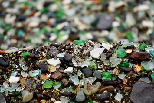 A piece of glass in the form of a heart on the beach. Multicolored glass on the beach. Wet multicolored glass on the beach of Vladivostok.