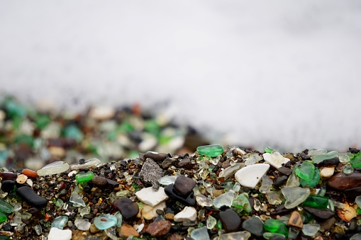 A piece of glass in the form of a heart on the beach. Multicolored glass on the beach. Wet multicolored glass on the beach of Vladivostok.