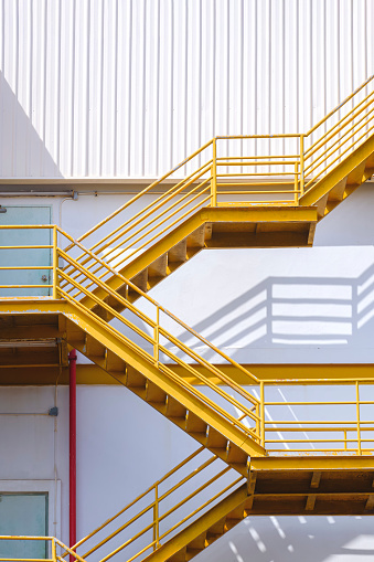 Yellow fire escape on white corrugated steel wall outside of industrial building in vertical frame.