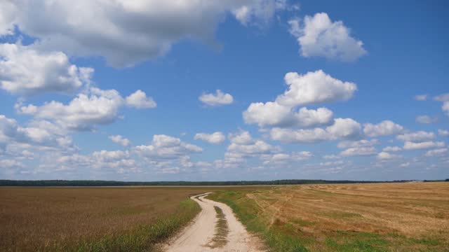 Rural Landscape With Field, Dirt Road And Blue Sky With Clouds