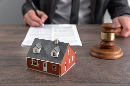 The hand of a judge with a gavel and a model of a house mediating property disputes in court, or property auctioneers.