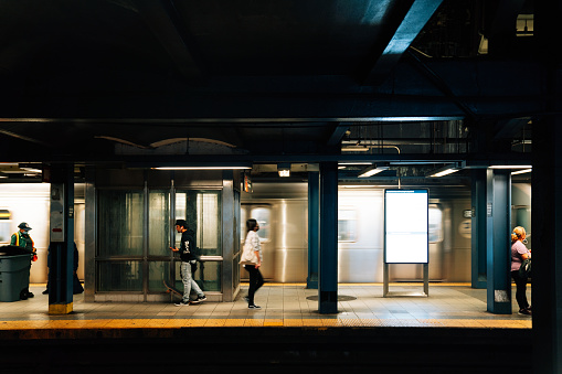 A train is passing in a subway in New York City. People are walking on the platform.