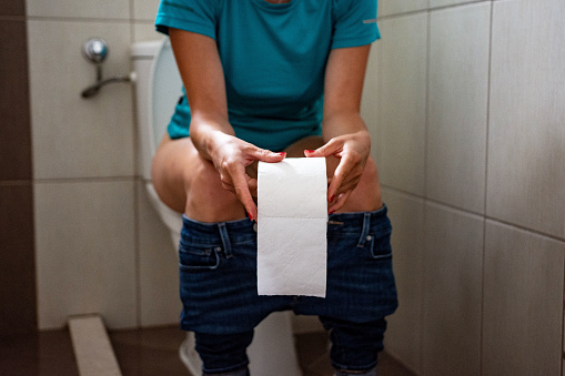 Woman sitting on toilet with toilet paper - constipation concept