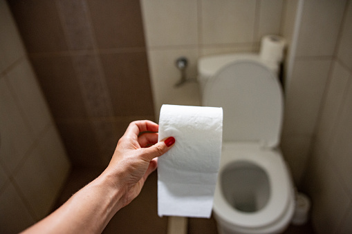 man with stomach issues sitting in toilet bowl and holding tissue roll in the bathroom