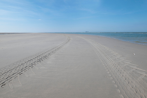 Perspective of tyre tracks on sandy beach with dark blue cloudy sky. High quality photo
